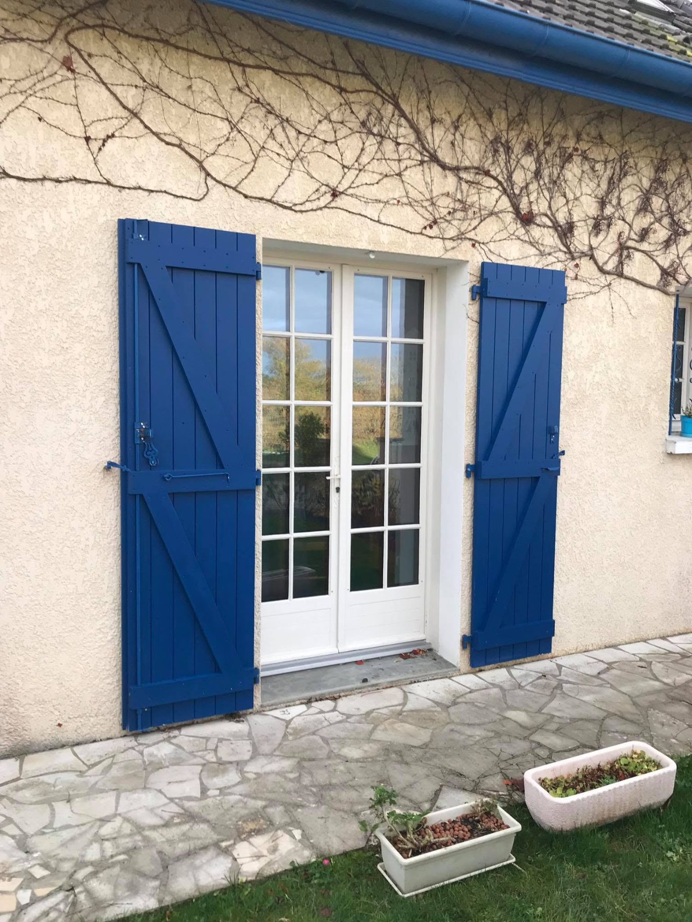Volets battants en Z, lasure bleue, encadrant une porte-fenêtre à petits bois